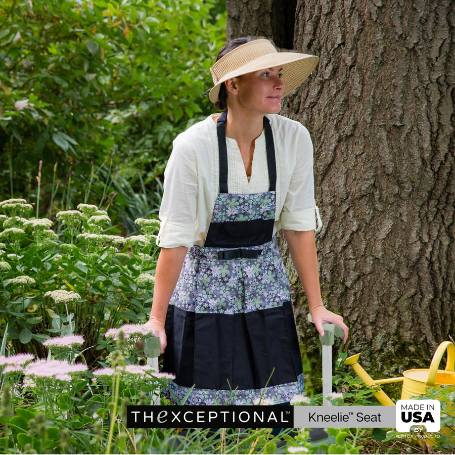 Woman in a garden with Kneelie Garden Kneeler wearing a floral apron and sun hat, holding gardening tools.